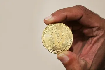 يد تمسك بعملة بيتكوين ذهبية